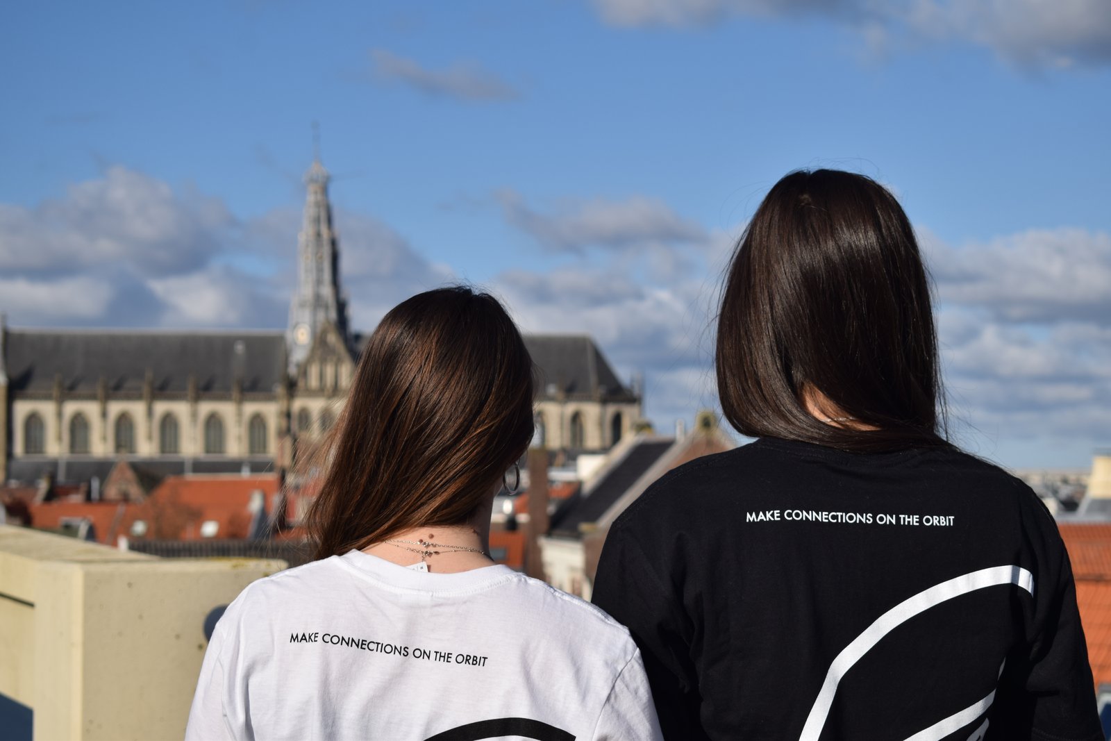 Two models in white and black SFERE t-shirts reading Make connections on the orbit