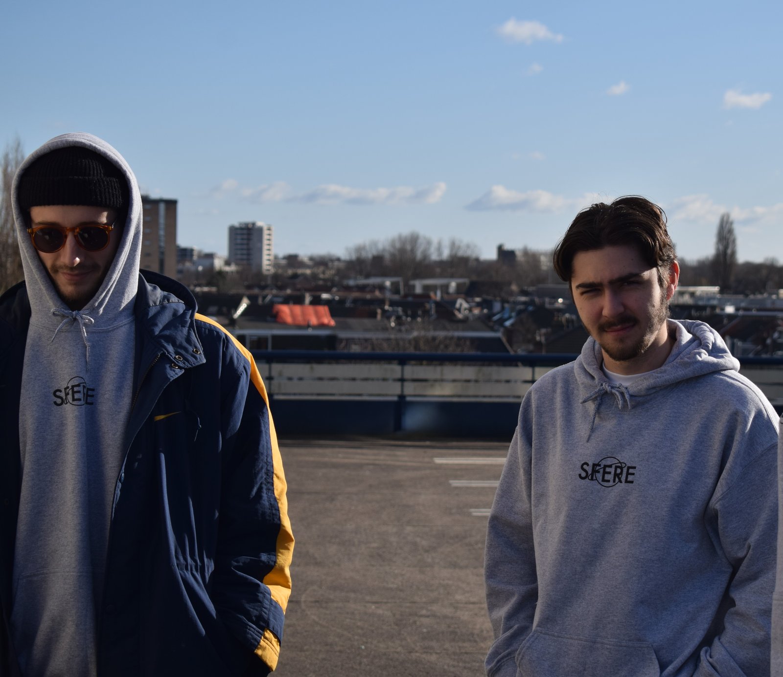 Two models in grey SFERE logo hoodies on a rooftop car park